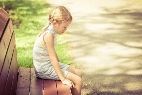 sad little girl sitting on bench in the park at the day time