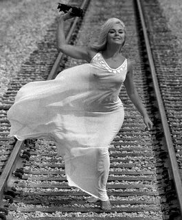 Elke Sommer holding a toy train running along real train tra