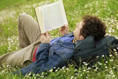Guy Laying On The Grass And Reading A Book Фотография, карти