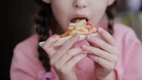 A little girl eats a slice of pizza in the restaurant Stock 