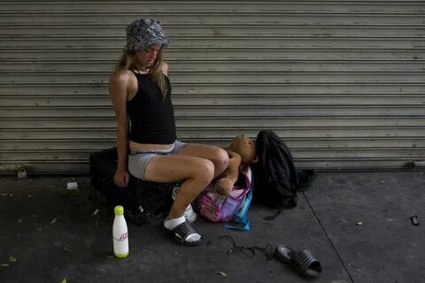 A young homeless woman, in a drug-induced state, wobbles whi