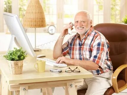 Happy old man on landline call. Sitting at desk using, compu