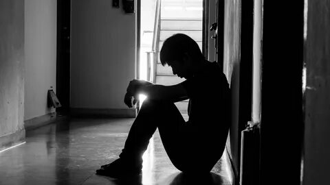 a sad young man sitting in the dark leaning against the wall