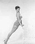 Debra Paget, in a striped swimsuit, leaning against the back