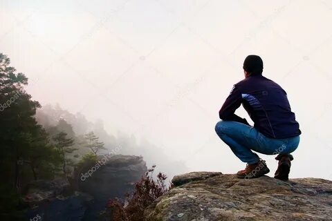 Hiker in squatting position on a rocky peak and enjoy the mi