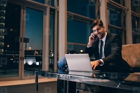 Smiling businessman with laptop talking on cellphone at the 