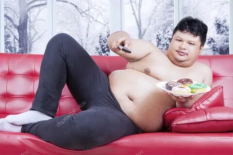 Overweight man watching tv and eats donuts Stock Photo by © 