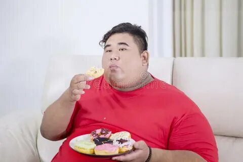 Portrait of Fat Asian Man Eating Doughnuts in Home Stock Ima