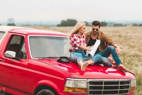 Travelling Young Couple Sitting on Car Engine Hood and Navig