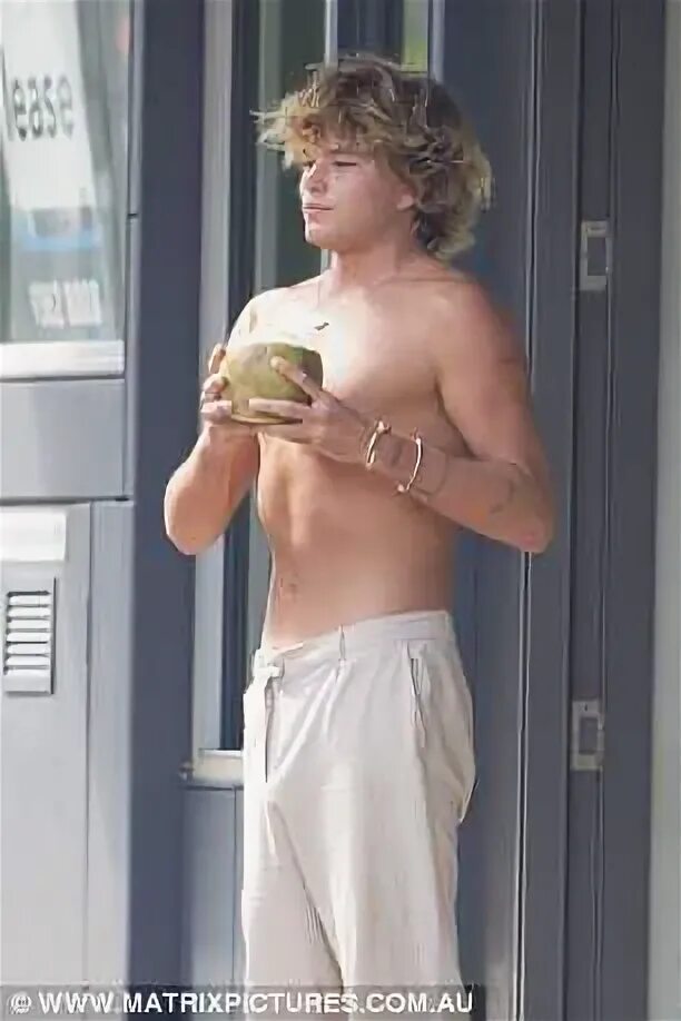 Jordan Barrett shirtless and barefoot as he drinks coconut w