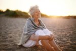 Cheerful old woman sitting on the beach - MOVE Communication