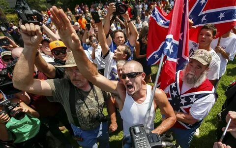 A Ku Klux Klan supporter waves a Confederate flag and yells at opponents at...