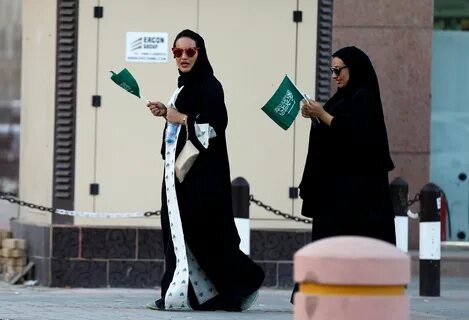 Saudi women hold national flags as they walk on a street dur