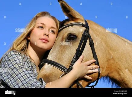 Teenage girl in equestrian helmet leading horse along paddock Stock Photo. 