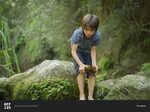Boy bending over to pick up large wet rock stock photo - OFF