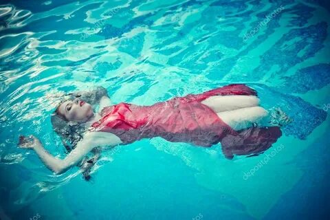 Junge sexy Frau, die im roten Kleid auf dem Swimmingpool sch