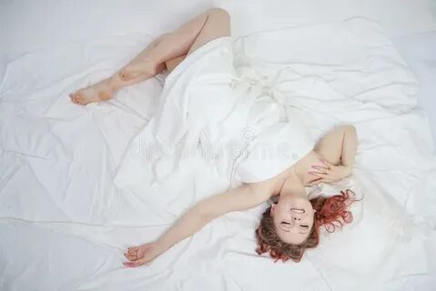 Красивая маленькая девочка лежит на белой кровати и наслажда