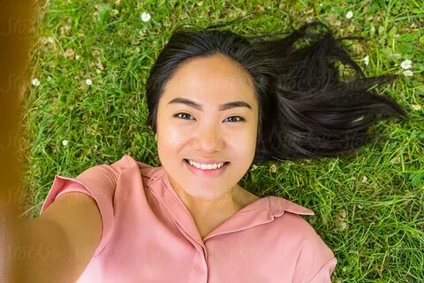 Young Filipino Woman Taking A Selfie While Lying Down On Gra