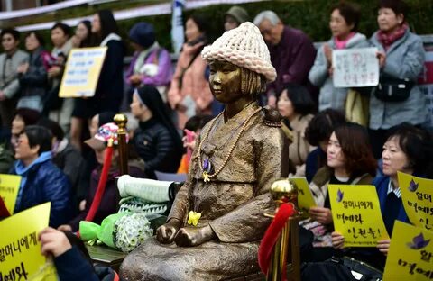 Protesters sit next to a statue of a South Korean teenage girl in tradition...