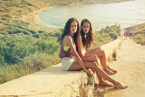 Two young brunette women in casuals sitting on the rock stairway near a bea