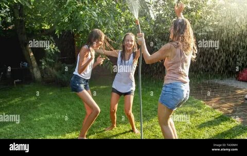 Image of cheerful laughing girls in wet clothes dancing in the garden and h...