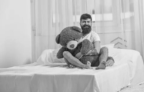 Guy on Cheerful Face Hugs Giant Teddy Bear. Man Sits on Bed 