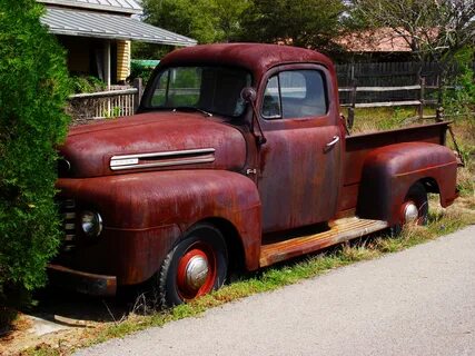 Old, rusty "Ford" truck car among the colorful plants in sun