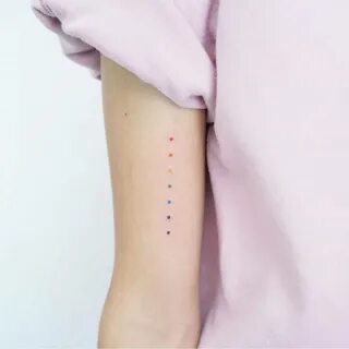 Minimalist rainbow dots tattoo on the bicep.