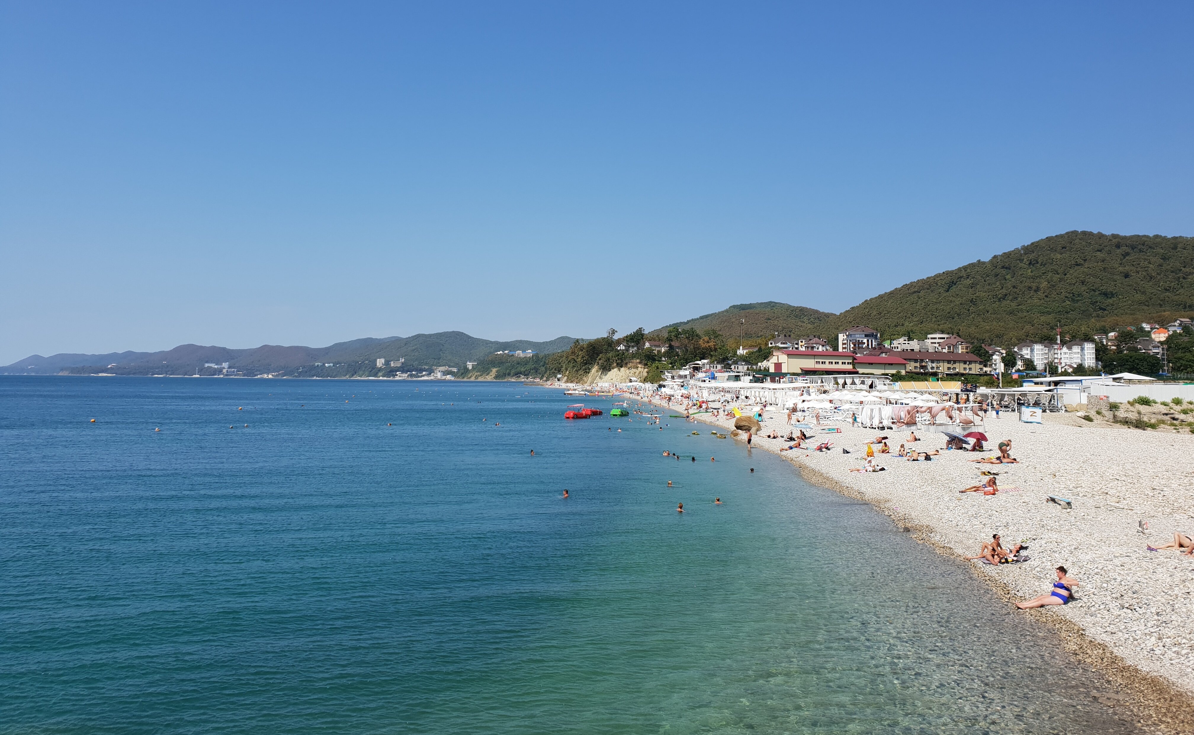 Галечный пляж в Агое с лежаками и зонтиками на фоне гор