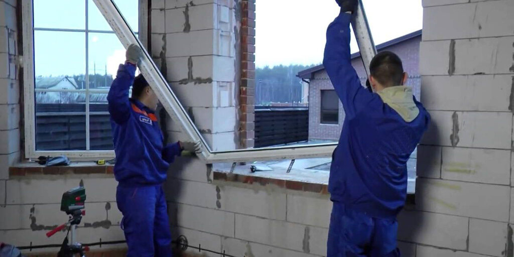 монтажник устанавливает пластиковое окно в кирпичном проеме