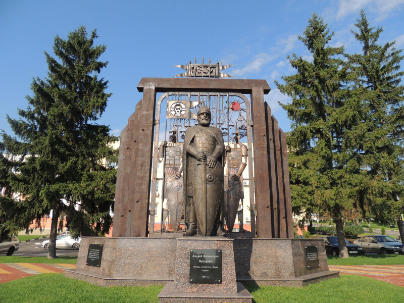 Бронзовая фигура воеводы Андрея Бутурлина в доспехах, стоящая на гранитном постаменте на фоне деревянного частокола.