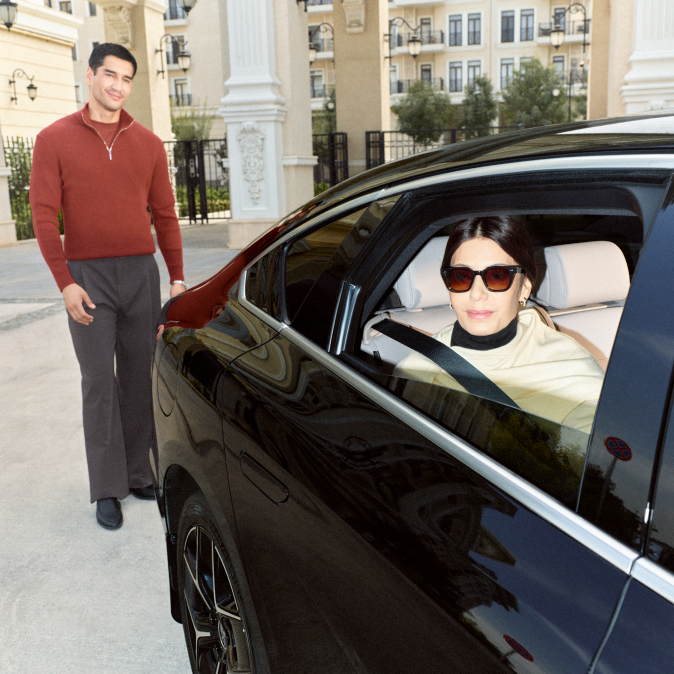 A young man waving goodbye to a woman driving away in a car