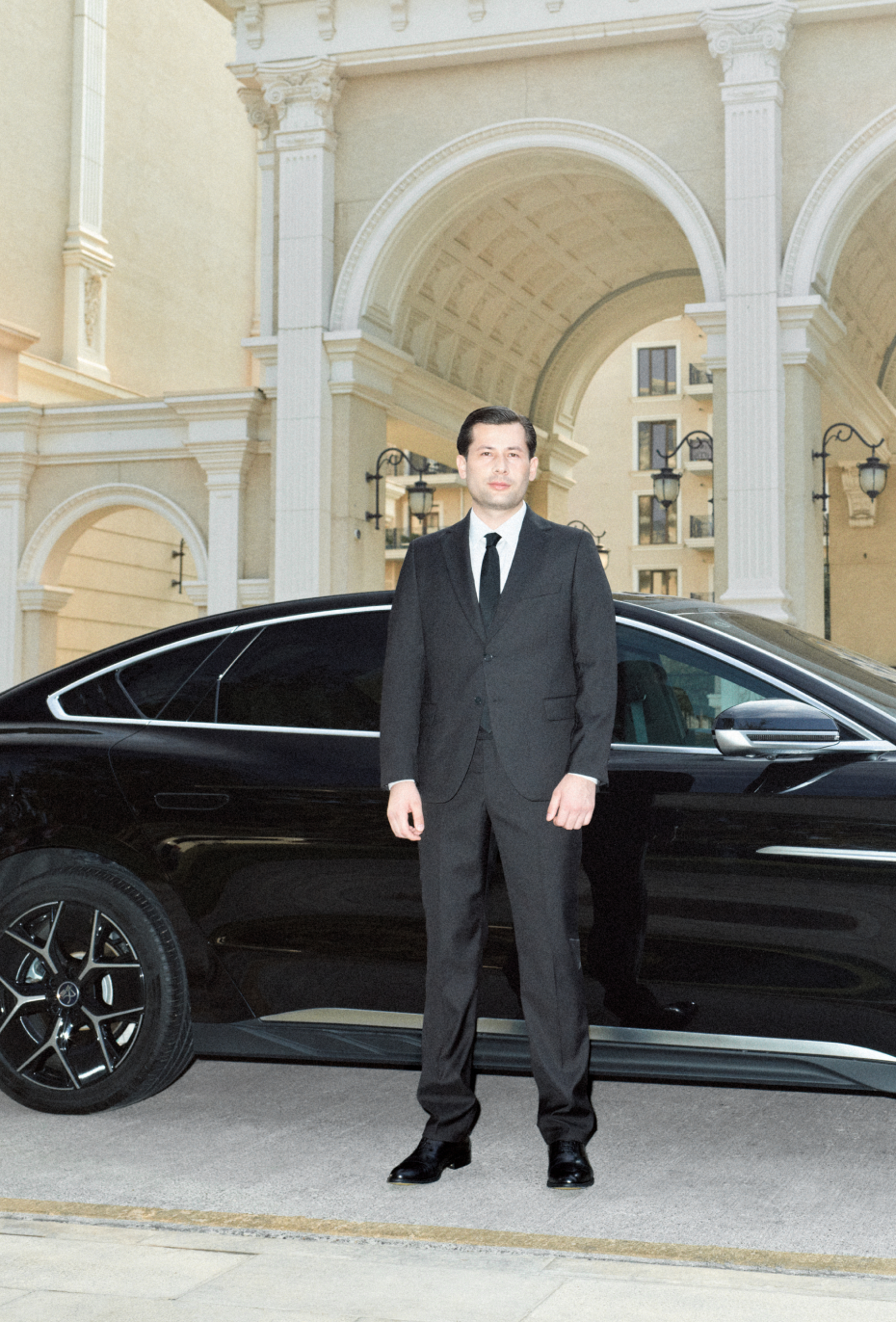 A driver in a business suit standing beside a car