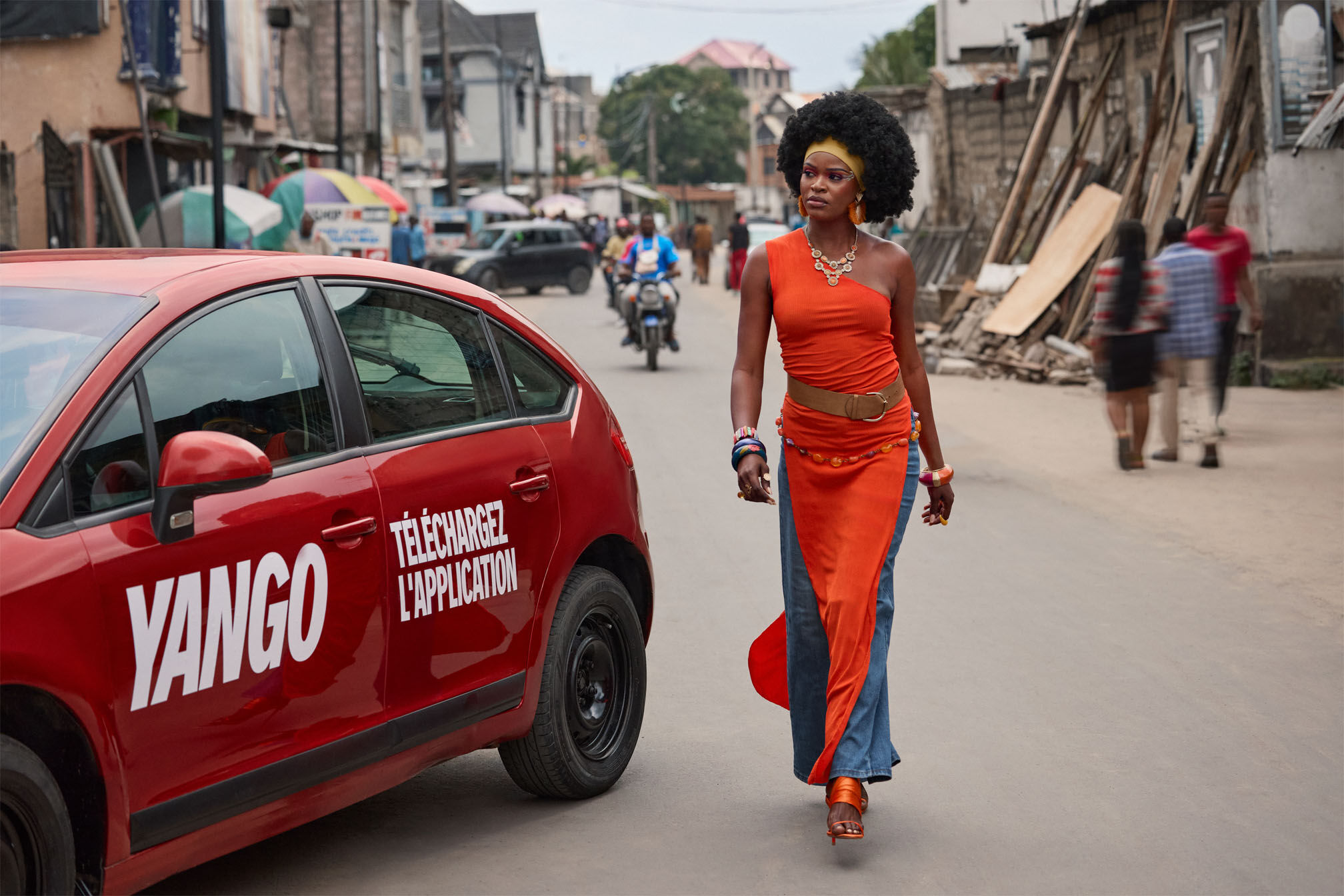 Woman in orange dress walking on street
Text on car: YANGO TÉLÉCHARGEZ L'APPLICATION