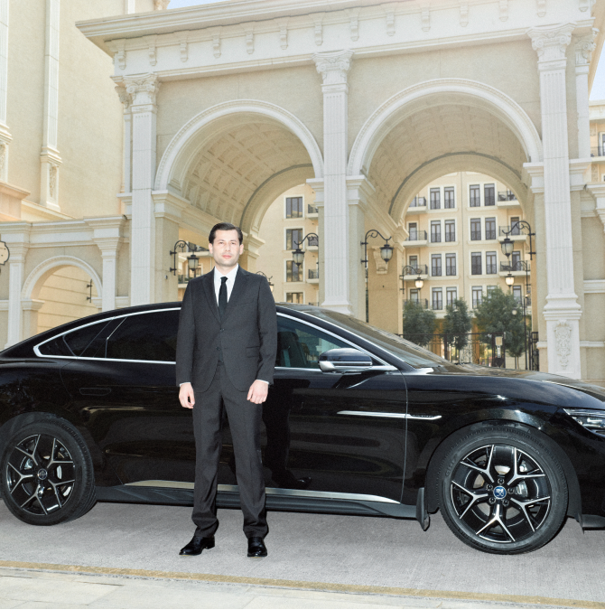 A driver in a business suit standing beside a car