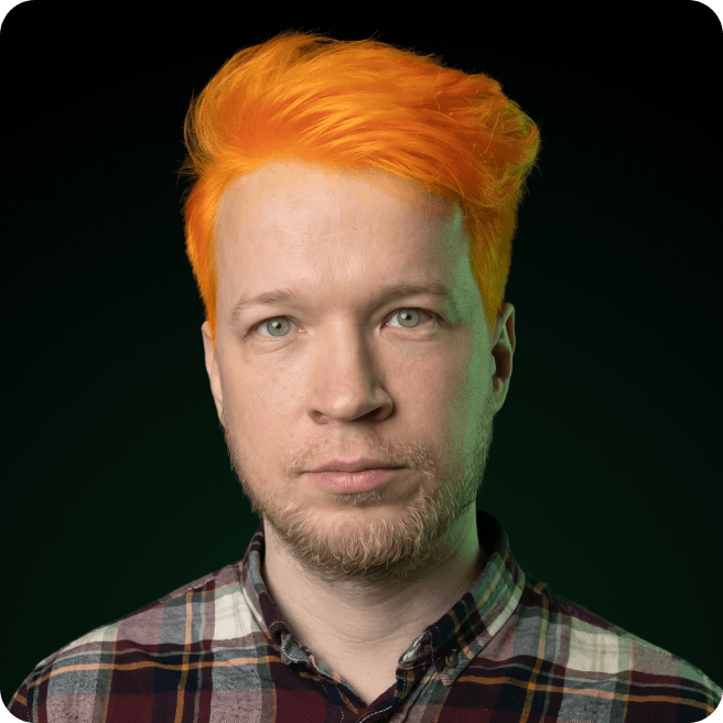 Man with bright orange hair, stubble, plaid shirt, dark background