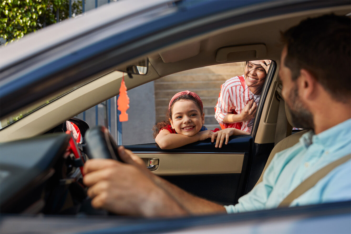 Familia en un auto, niña y mujer sonriéndo, hombre con volante