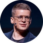 Мужчина с короткими волосами, в очках и тёмном пиджаке, с микрофоном у уха