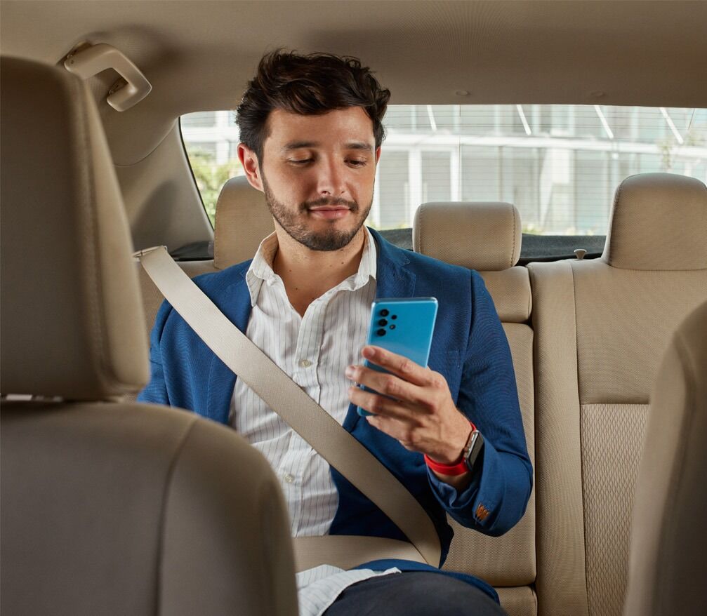 Hombre en blazer azul usando cinturón de seguridad y mirando smartphone en el asiento trasero de un auto