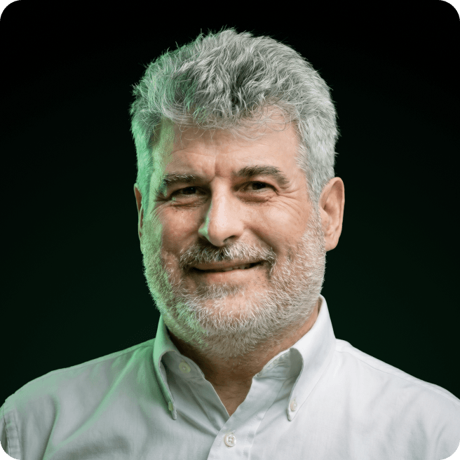 Man with gray hair and beard, wearing a white shirt, smiling slightly