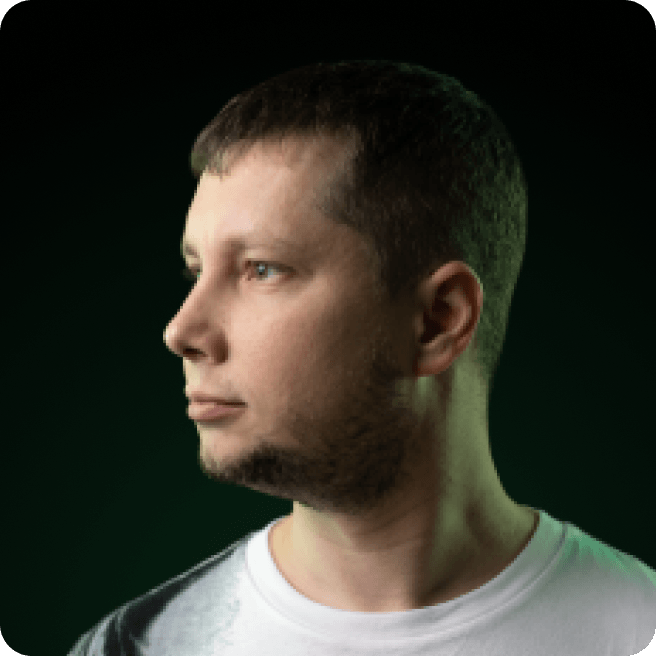 Man with short dark hair, stubble, in white t-shirt, side profile, dark background