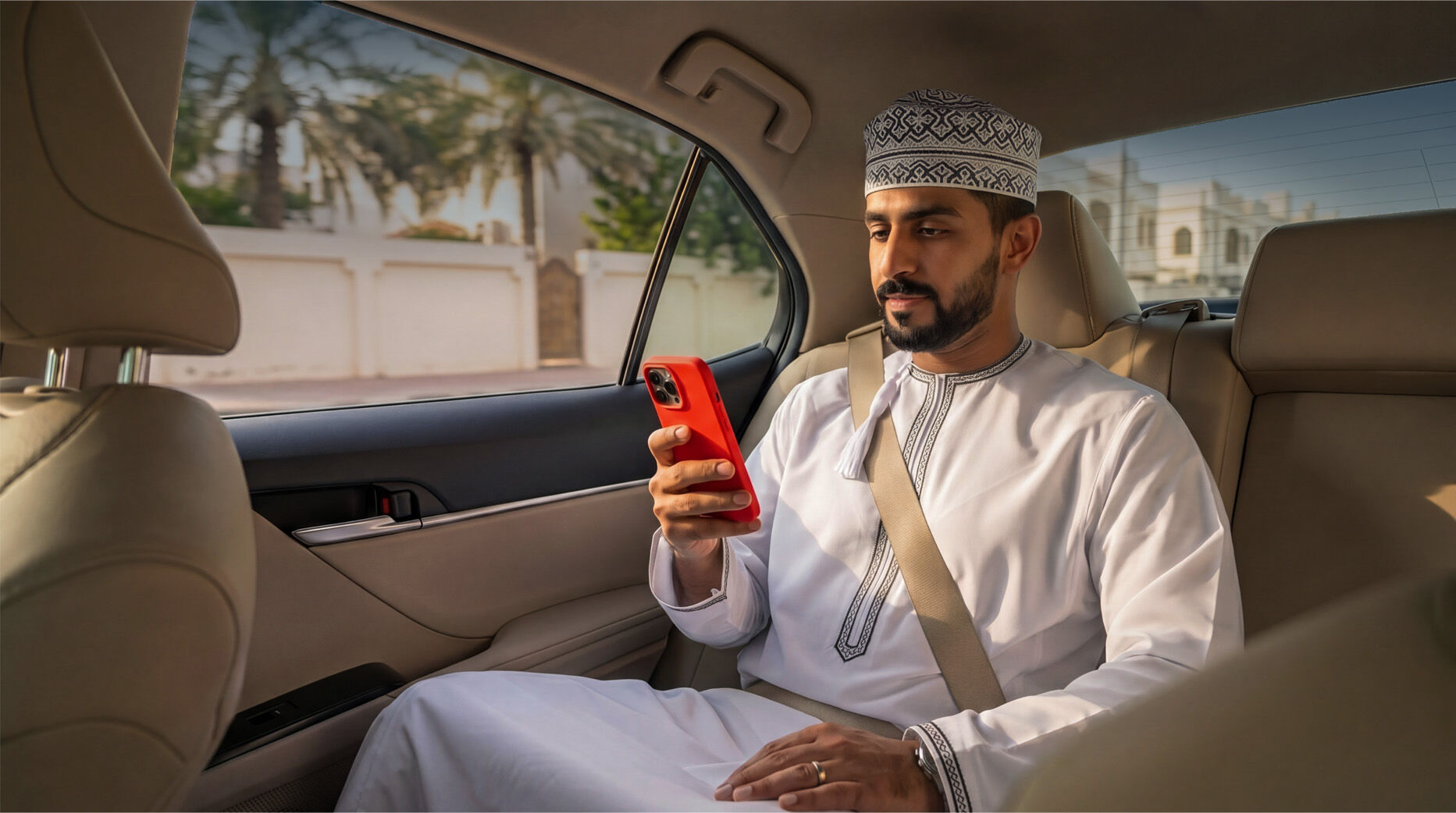 Man in traditional white outfit holding red phone in car