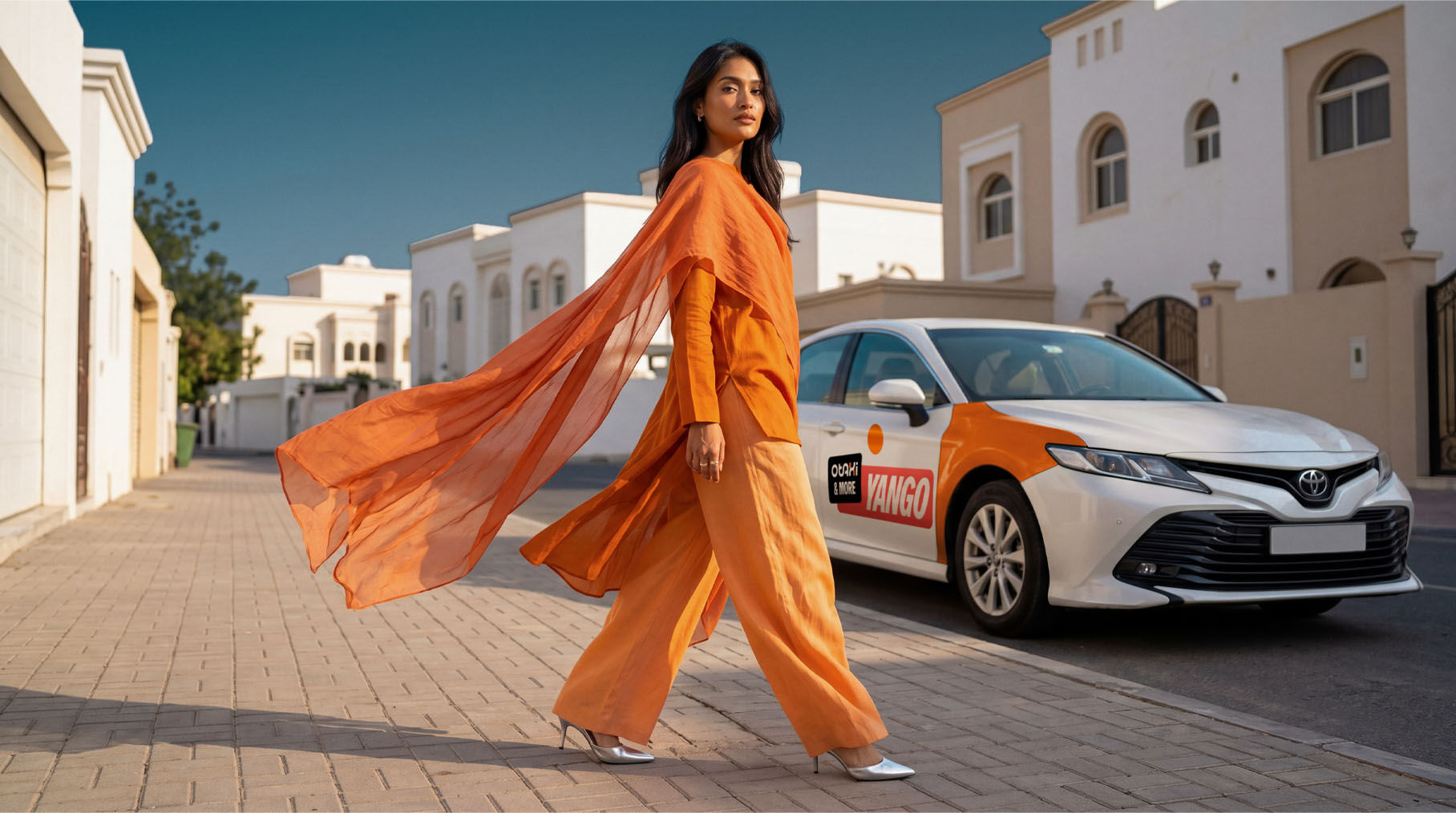 Woman in flowing orange outfit walking past white Toyota car with YANGO logo
