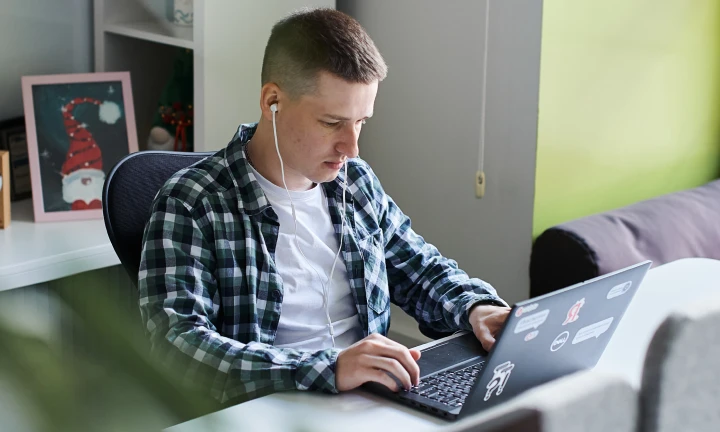 Молодой человек работает на ноутбуке, в наушниках