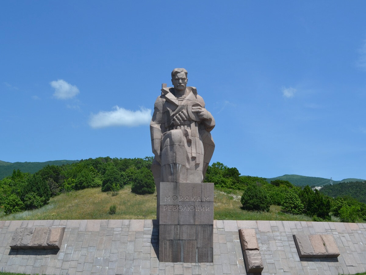 Моряк снял бескозырку, преклоняет колено и смотрит вдаль, печально провожая тонущие корабли