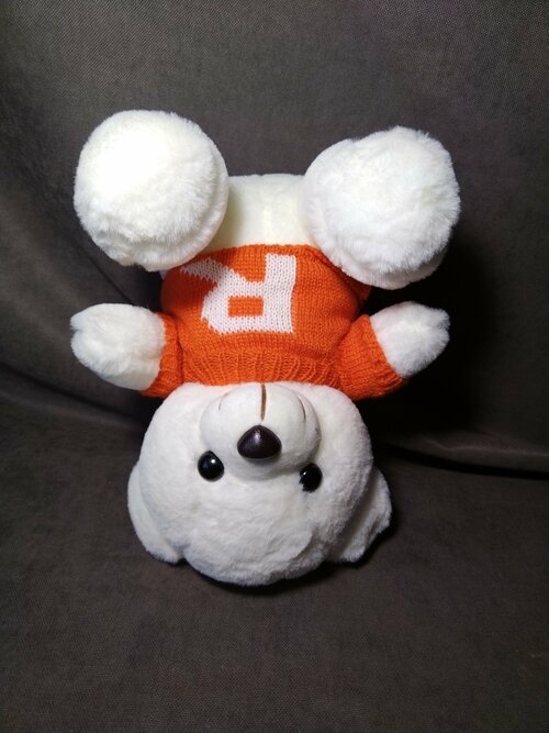Мишка плюшевый белый сидит в оранжевом свитере с буквой 
