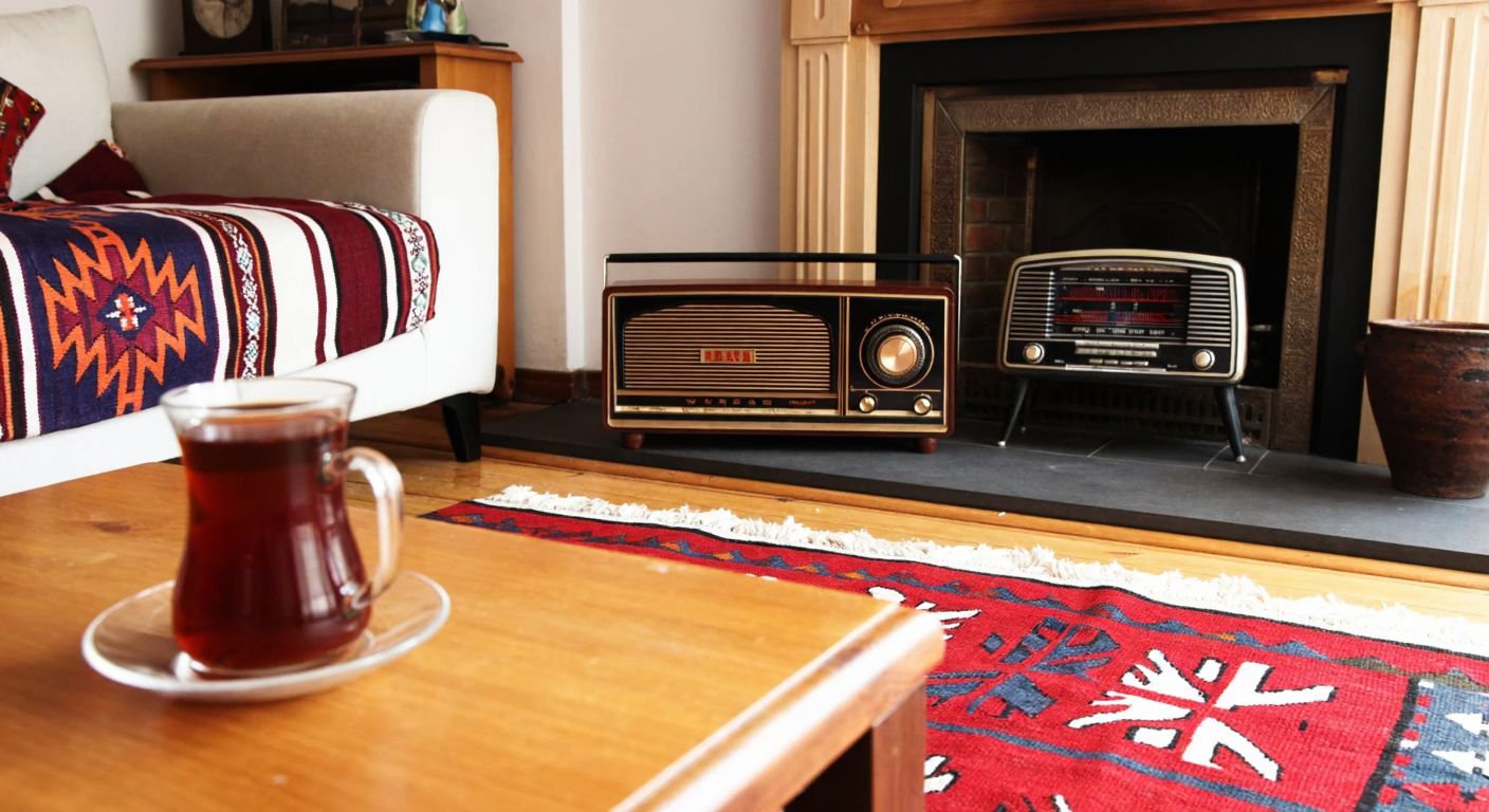 A cozy Turkish living room in Kırşehir with a traditional kilim rug, a vintage radio playing folk music, and a steaming cup of çay on a wooden table.