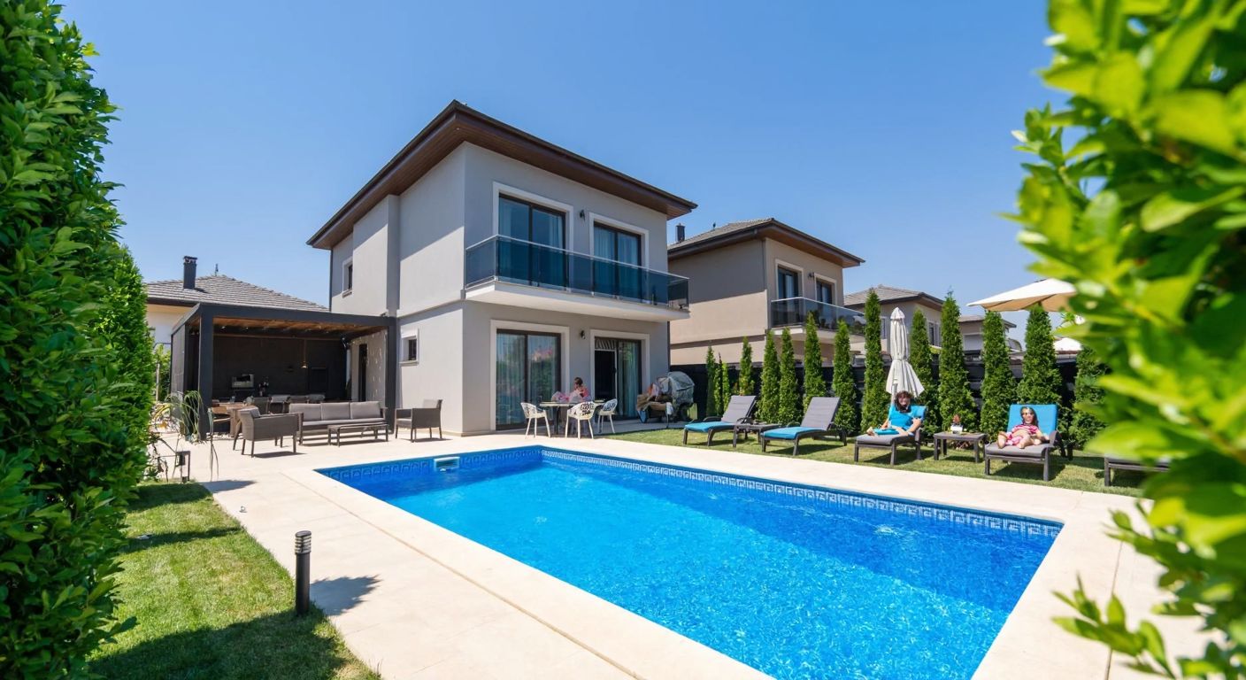 A sunlit modern villa with a sparkling blue pool in the garden, nestled near the Porsuk River in Eskişehir, surrounded by lush greenery and a relaxed family enjoying the outdoor space.