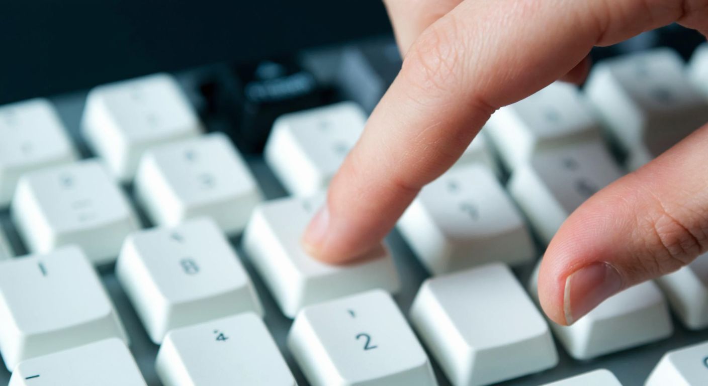 A close-up of a left hand hovering over a keyboard, with the ring finger extended toward the number "2" key, against a blurred background of other keys.