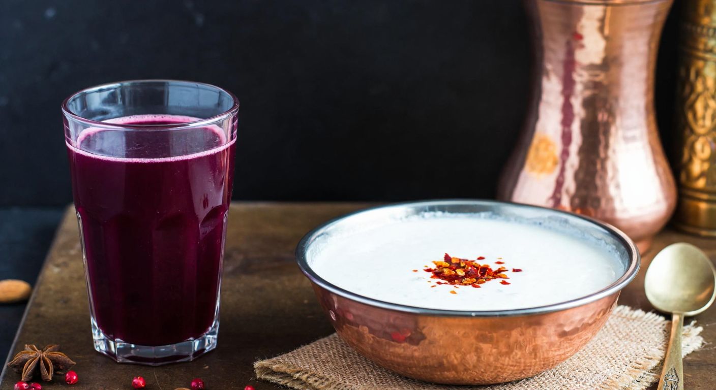 A rustic Turkish kitchen counter with a glass of deep purple şalgam suyu and a bowl of creamy white ayran being mixed together in a copper bowl, garnished with a sprinkle of red pul biber.